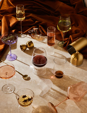 The Blush pink wine glass by Estelle Colored Glass lays on a marble table with other colored wine glasses