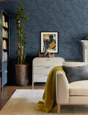The Aimee mohair mustard yellow wool throw blanket with fringe ends lays on a beige linen sofa in a living room with indigo patterned walls and an indigo throw pillow