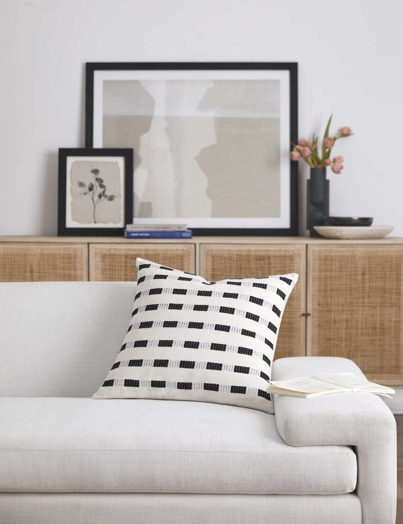#color::onyx | Bertu onyx black pillow with a woven dash pattern by Bolé Road Textiles sits on a white sofa with a rattan cane sideboard in the background