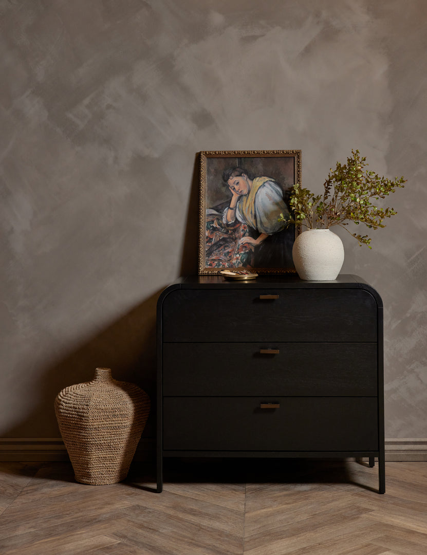 #color::black | The Brooke 3-drawer black oak dresser sits against a gray wall next to a jute basket with a portrait and a white vase