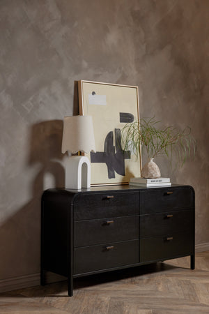 The the brooke black oak 6-drawer rounded dresser sits in a room with a sculptural lamp and wall art atop it