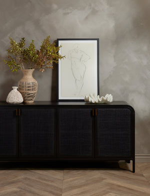 The Brooke black solid oak sideboard sits against a gray wall with a woven vase, ruffle bowl, and portrait wall art sitting atop it
