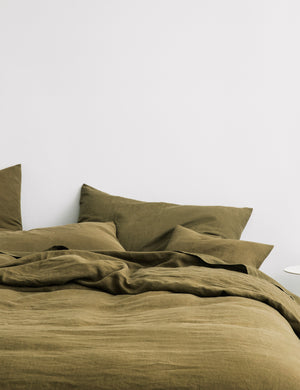 The European Flax Linen olive green Duvet Cover by Cultiver lays on a bed with other cultiver linens