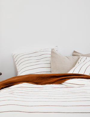 The European Flax Linen cedar orange stripe Duvet Cover by Cultiver lays on a bed with other cultiver linens
