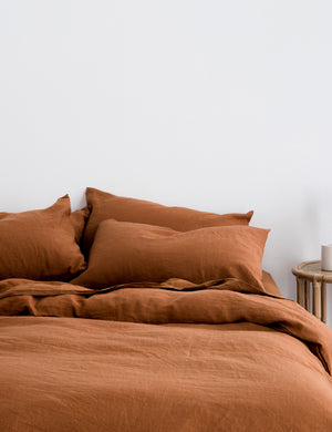 The European Flax Linen cedar orange Duvet Cover by Cultiver lays on a bed with other cultiver linens