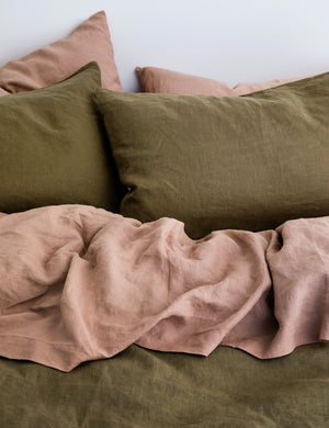 The European Flax Linen fawn pink Sheet Set by Cultiver lays on a bed with olive green linens