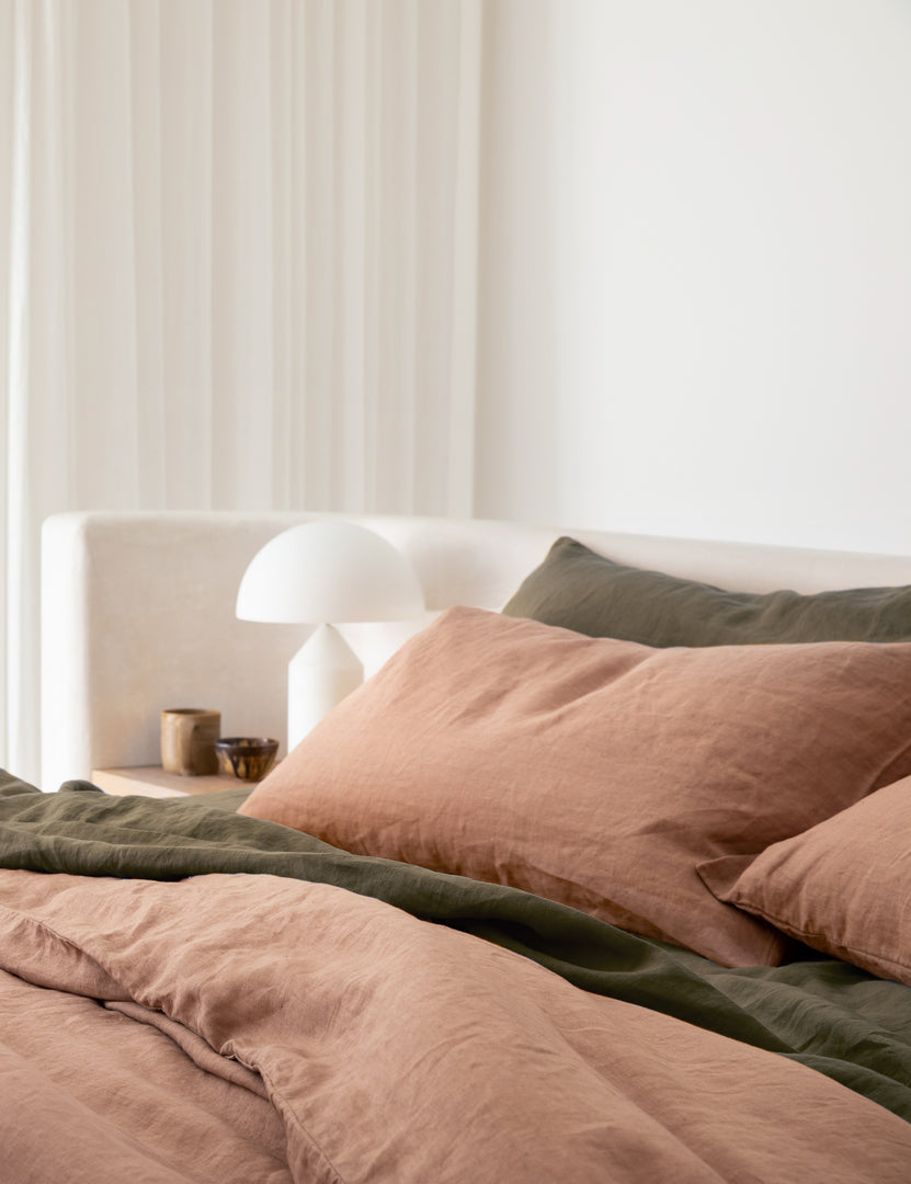 #color::fawn #size::standard #size::king | The set of two european flax linen fawn pink pillowcases by cultiver lay on a bed with olive green cultiver linens