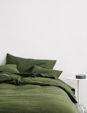The European Flax Linen forest green Duvet Cover by Cultiver lays on a bed with other cultiver linens