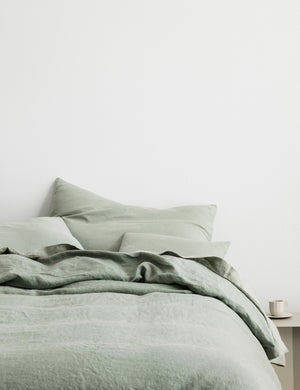 The European Flax Linen sage green Duvet Cover by Cultiver lays on a bed with other cultiver linens
