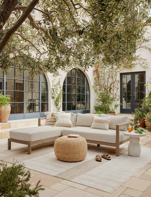 The valencia indoor and outdoor rug lays in an outdoor space under a sectional sofa and a woven ottoman