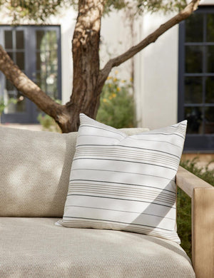 The Whitehaven indoor and outdoor square pillow sits on a gray linen sofa in an outdoor space