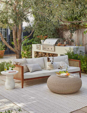The Clouded White Round Side Table sits on a patio next to a woven sofa and round woven coffee table
