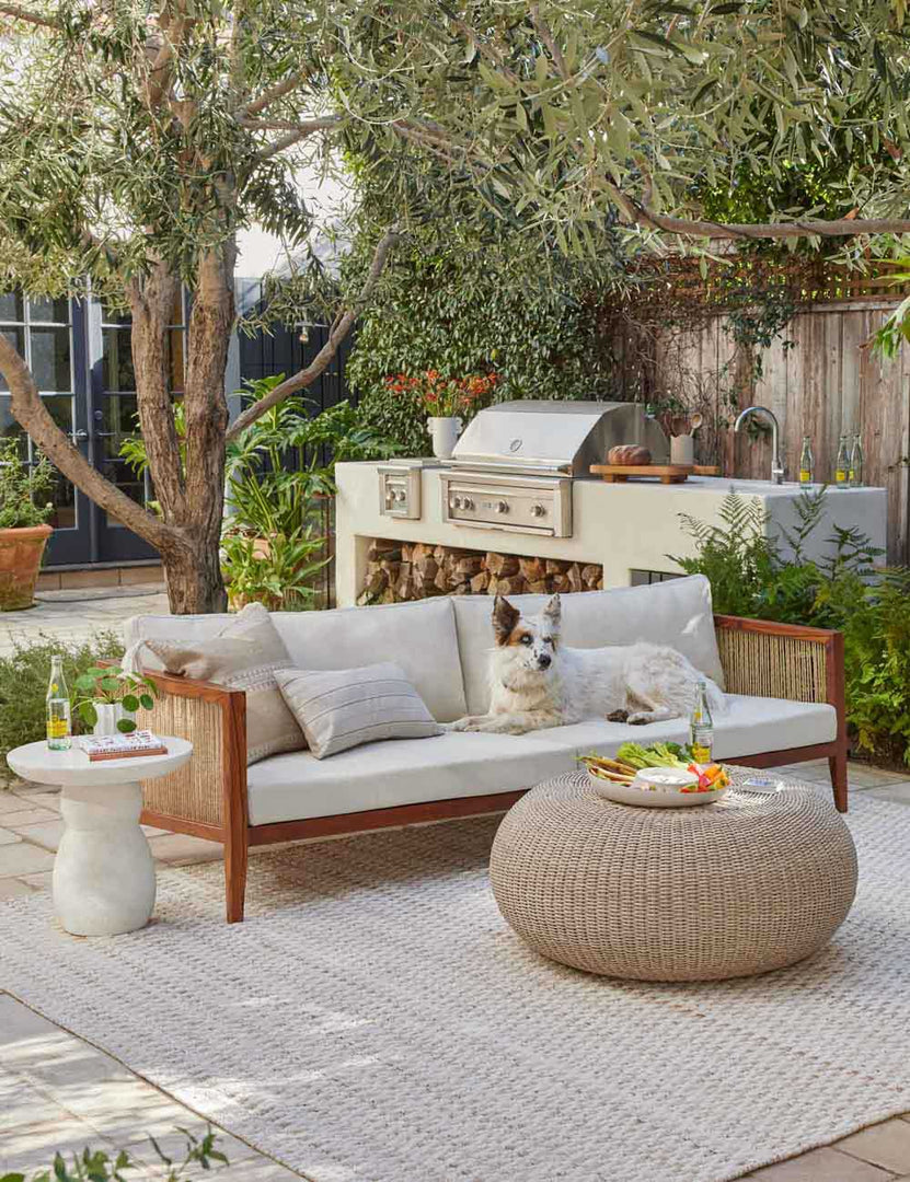 | The Clouded White Round Side Table sits on a patio next to a woven sofa and round woven coffee table
