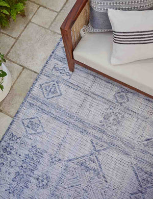 The Yamina blue indoor and outdoor rug lays under a wood-framed sofa that has two striped throw pillows atop it