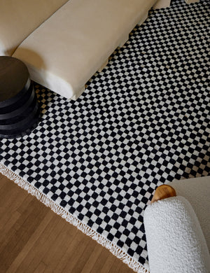 Bird's-eye view of the Black and white Checkerboard Rug by Sarah Sherman Samuel underneath a boucle accent chair, black side table, and brie velvet sofa