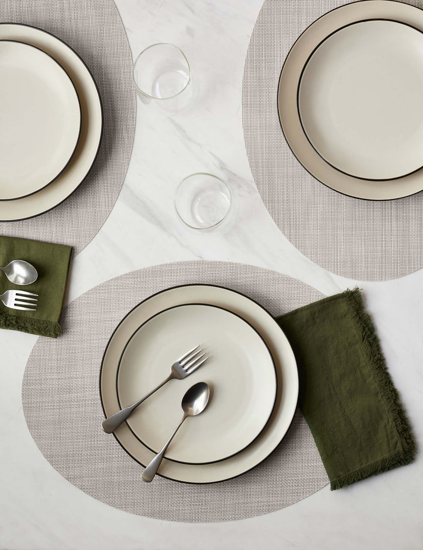 #color::parchment | The Set of four parchment-toned Mini Basketweave Oval Placemat by Chilewich sits under a cream dinnerware set