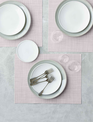 The Set of four blush pink Mini Basketweave Rectangle Placemat by Chilewich sits under a white dinnerware set