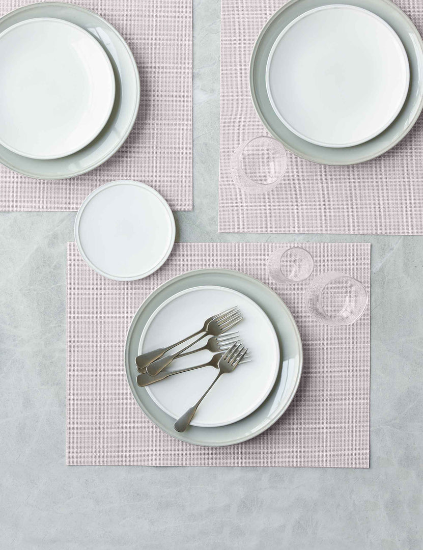 #color::blush | The Set of four blush pink Mini Basketweave Rectangle Placemat by Chilewich sits under a white dinnerware set