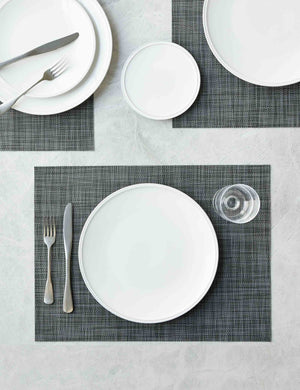 The Set of four cool gray Mini Basketweave Rectangle Placemat by Chilewich sits under a white dinnerware set