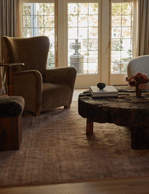 The Chiltern mauve rug lays in a dark living room under a linen sofa, a round wooden coffee table, and a brown accent chair