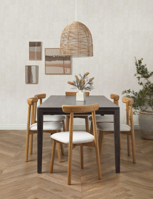 The Beehive jute woven pendant light is hung above a black rectangular dining table that is surrounded by six dining chairs