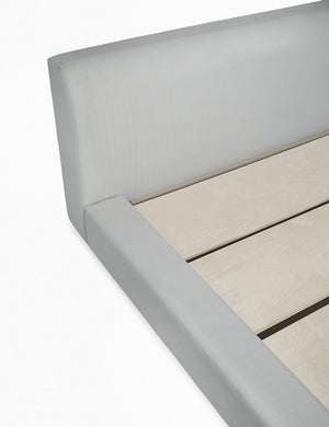 Close-up of the left side of the Clayton gray upholstered platform bed featuring the headboard, side paneling, and wooden support beams