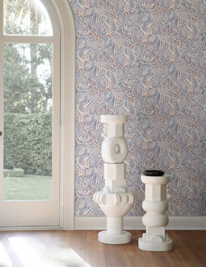 The Bequia Ocean Wallpaper is in a bright room with an arched french door and two white pedestal decorative objects