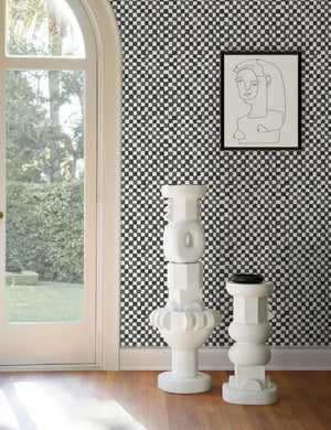 Black and ivory Checkerboard Wallpaper by Sarah Sherman Samuel is in a room with two white pedestals and an abstract portrait wall art