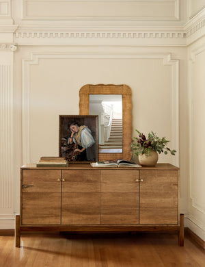 Yarely woven rattan frame wall mirror styled on a sideboard cabinet with artwork and decorative books.