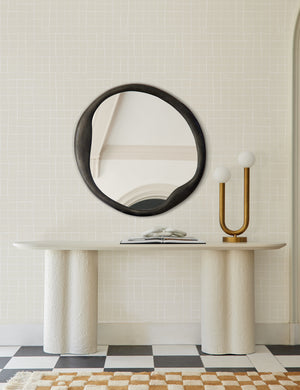 The Doreen black organic round mirror is hung in an entryway against a gray patterend wall and above a white sideboard and a white and black checkered floor