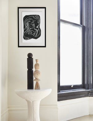 The Hold Print in a black frame is hung next to a large window above a white side table with two sculptural objects