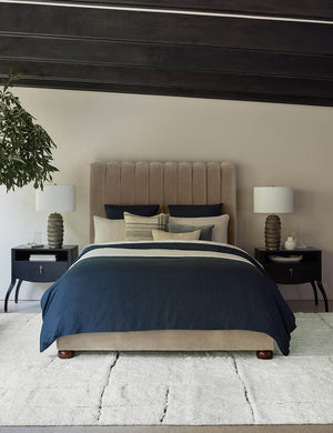 The costa rug lays in a bedroom under two black nightstands and a beige velvet bed with navy and ivory linens