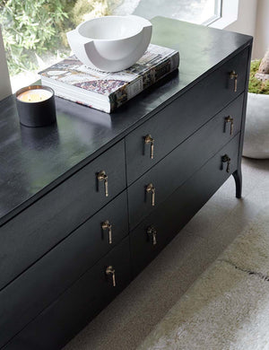 Angled view of the Anabella black wood dresser with silver drawer with a book, white centerpiece bowl and candle sitting atop it.