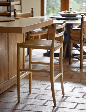 Side view of the Nicholson slim natural oak wood frame and woven seat counter stool at a kitchen counter.