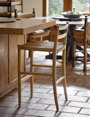 #color::natural-oak | Side view of the Nicholson slim natural oak wood frame and woven seat counter stool at a kitchen counter.