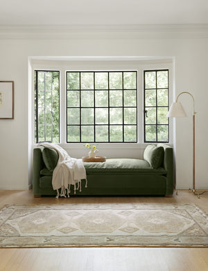 The Minerva rug lays in a bright room under a gray velvet daybed that is under three black-framed windows