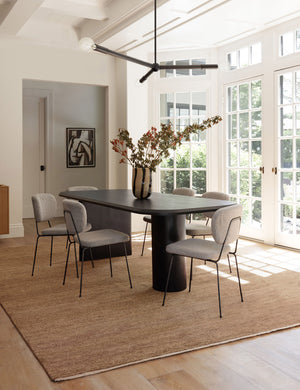 The Heritage wheat rug lays in a dining room with wrap-around windows, a black dining table, and upholstered dining chairs