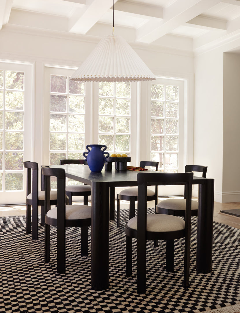 #color::black | Six Tobie Dining Chairs sit around a black rectangular dining table with a blue centerpiece vase atop a checkered rug