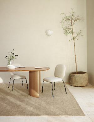 The Heritage moss gray rug lays in a dining room under a wooden dining table and two ivory dining chairs with sculptural legs
