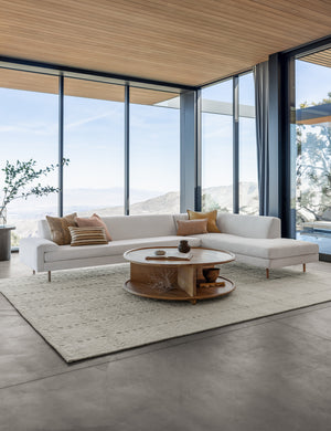 The Estee white linen right-Facing Sectional Sofa sits atop a textured white rug in a room with floor to ceiling windows
