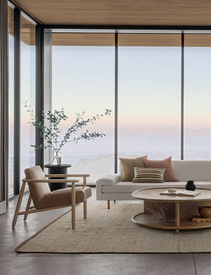 The Khloe natural rug lays in a living room with wrap around floor to ceiling windows under an ivory sofa