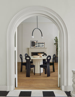 The Doric white round dining table sits in a dining room surrounded by black wooden sculptural chairs