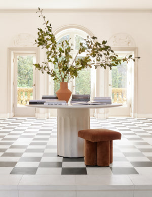 The Doric white round dining table sits in a bright room with an arched french door and black and white checkerboard floors