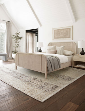 The esha rug lays in a bedroom with sloped ceilings under a white-washed woven bed and a whitewashed nightstand