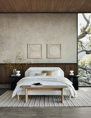 The Kipp talc linen platform bed sits in between two round black nightstands atop a textured ivory rug