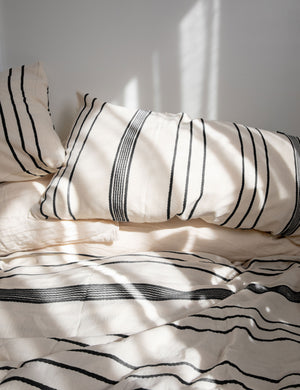 The Marlo Cotton hand loomed black striped Duvet Set by House No. 23 lays on a bed in a sunny bedroom