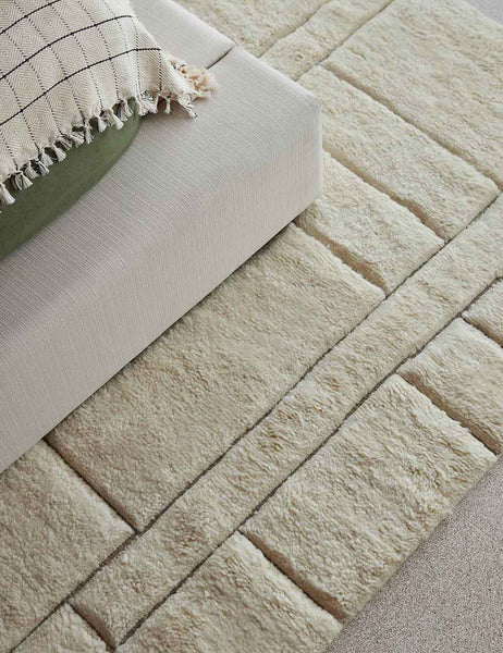 #size::6--x-9- #size::8--x-10- #size::9--x-12- #size::10--x-14- #size::12--x-15- | The Maleena cream hand-knotted wool and cotton area rug with abstract line tufting sits under a linen upholstered platform bedframe.