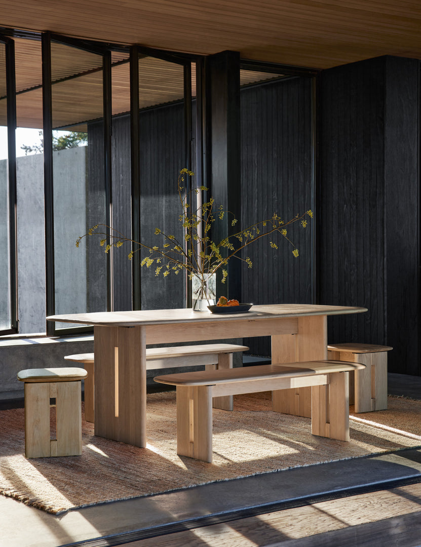 | The Henrik light wood bench sits on both sides of a dining room table in a room with black-wooden walls 