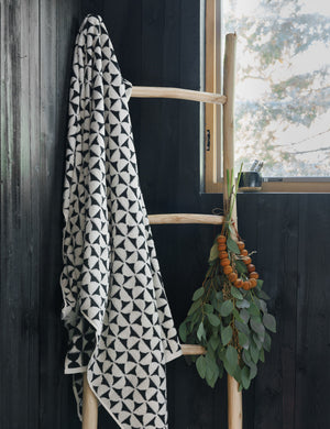 The Harper black and white towel by house number 23 with half-moon designs is hung on a wooden ladder in a room with black wooden walls