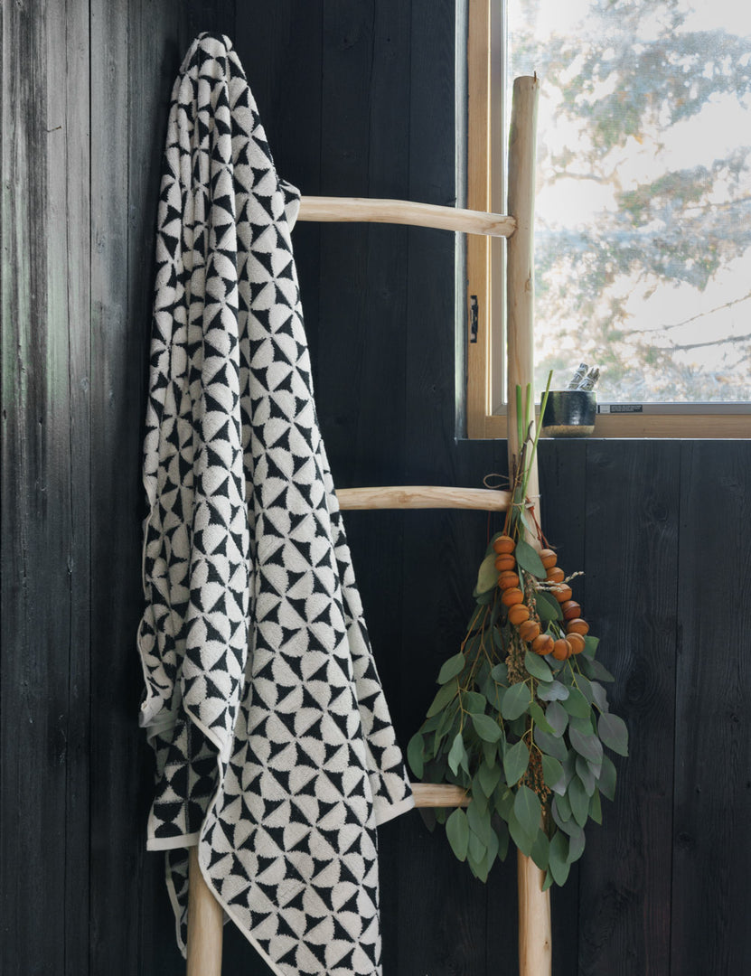 #color::meteorite | The Harper black and white towel by house number 23 with half-moon designs is hung on a wooden ladder in a room with black wooden walls